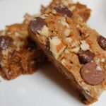 a white plate with 2 blondie bars, studded with chocolate hips and almonds