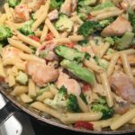 a partial photo of a skillet with a penne pasta dish with broccoli, chicken, and flecks of sun-dried tomato